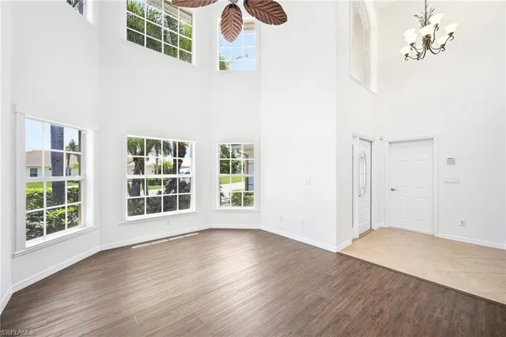 Double-height living space featuring expansive multi-pane windows, wood-finish flooring, and a decorative ceiling fan