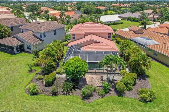 Aerial perspective showcasing the property's expansive backyard, featuring a screened-in pool enclosure, mature tropical landscaping, and a paver patio