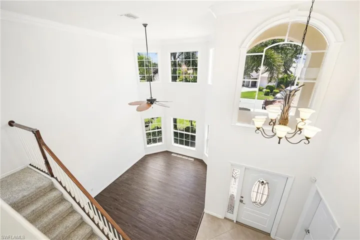 Two-story entryway featuring high ceilings, wood-finish flooring, a traditional chandelier, a decorative front door with sidelights, and multiple windows including an arched upper window
