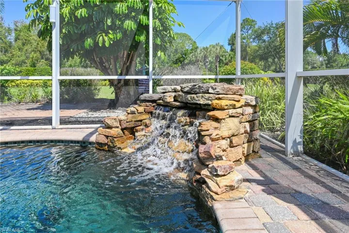 Screened pool enclosure featuring a natural stone waterfall, brick paver decking, and a tiled pool edge