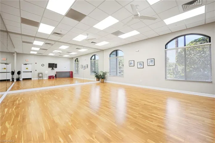Spacious interior featuring wood-finish flooring, a mirrored wall, and arched windows with horizontal blinds