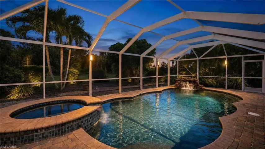 Screened swimming pool enclosure featuring a waterfall, integrated spa, and paver decking