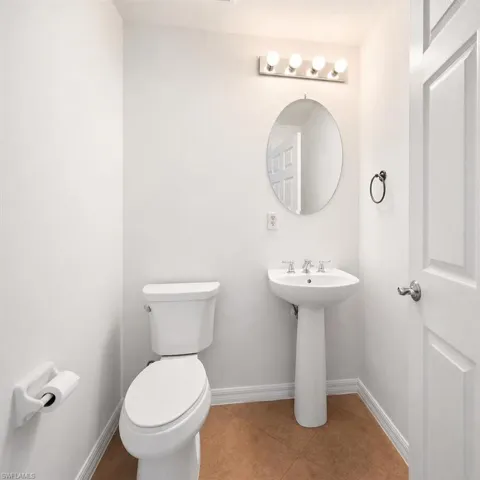 White pedestal sink with a chrome faucet, oval mirror, and contemporary vanity lighting