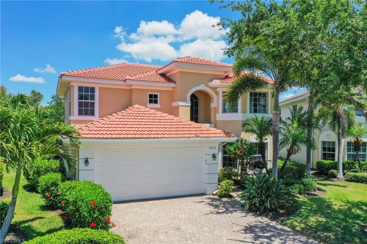 Two-story stucco residence featuring a terracotta-tiled roof, an integrated two-car garage with a paneled door, and a paver driveway