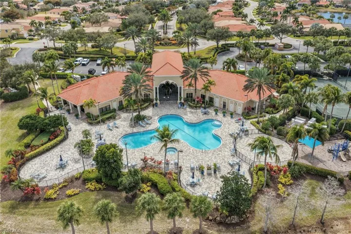 Expansive community clubhouse featuring a large swimming pool, surrounding patio, lush landscaping, and tennis courts