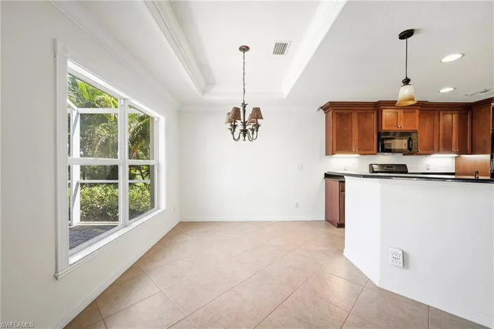 Open-concept living space featuring a tray ceiling, tile flooring, and a large window overlooking lush foliage