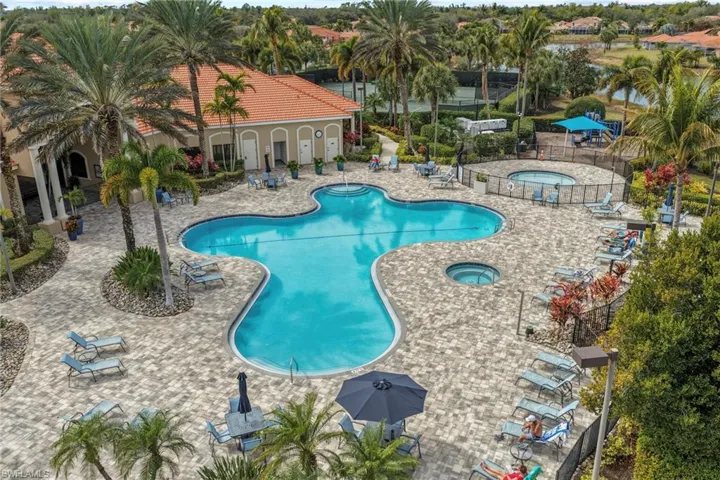 Resort-style pool area featuring a freeform swimming pool, two integrated hot tubs, a surrounding paver deck, and extensive tropical landscaping