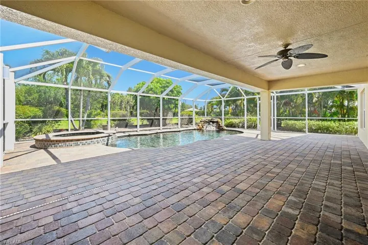 Screened lanai featuring extensive paver decking, a freeform swimming pool with waterfall feature, and an integrated spa with mosaic tile accents