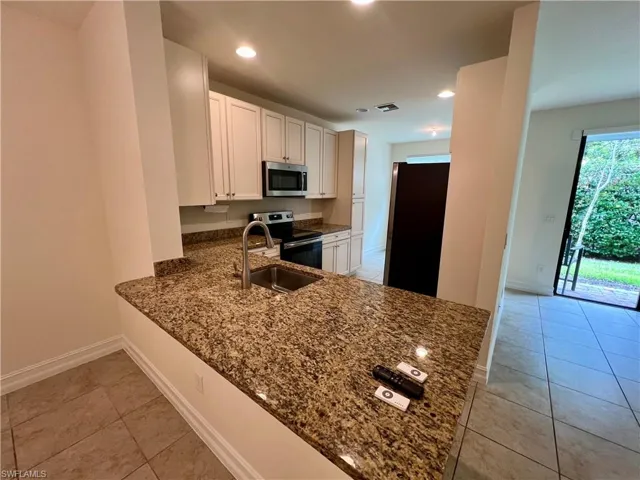Kitchen with appliances with stainless steel finishes, dark stone counters, sink, light tile patterned flooring, and white cabinetry