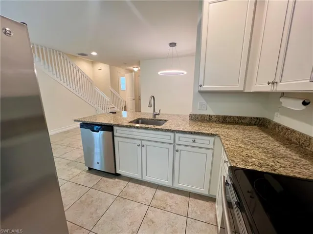 Kitchen with decorative light fixtures, stainless steel dishwasher, white cabinetry, range, and light tile patterned floors