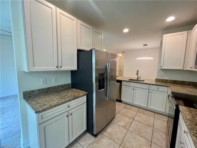Kitchen featuring light tile patterned flooring, decorative light fixtures, white cabinetry, sink, and appliances with stainless steel finishes