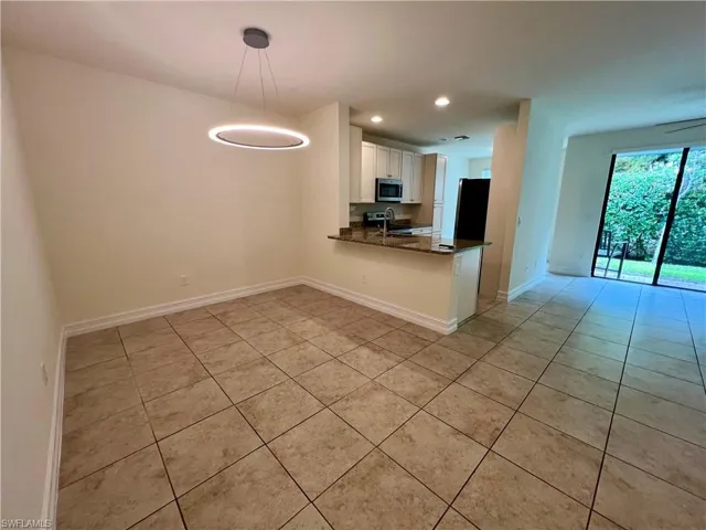 Kitchen featuring light tile patterned floors, kitchen peninsula, white cabinets, decorative light fixtures, and sink