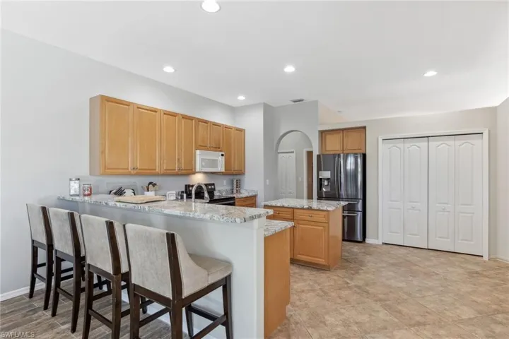 Kitchen with white microwave, a kitchen island, a peninsula, electric stove, and stainless steel fridge