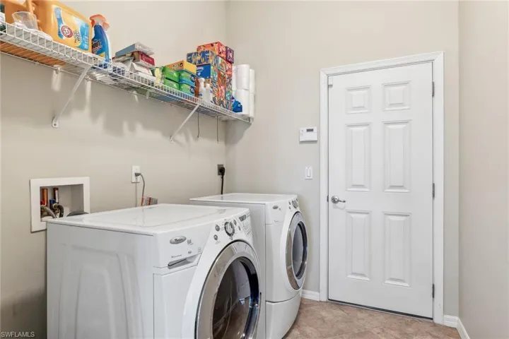 Washroom featuring laundry area, light tile patterned flooring, washing machine and dryer, and baseboards