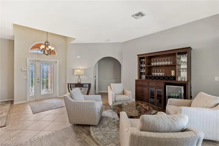 Living room featuring visible vents, arched walkways, an inviting chandelier, light tile patterned floors, and a dry bar