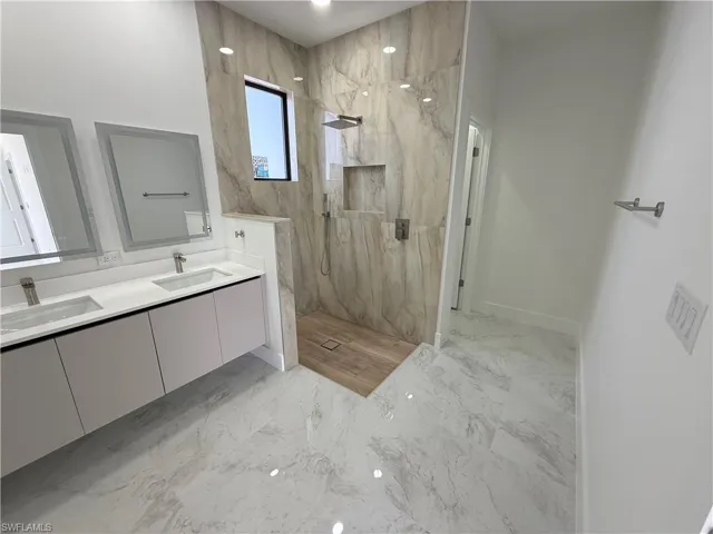 Bathroom featuring double vanity, light marble finish flooring, and a marble finish shower