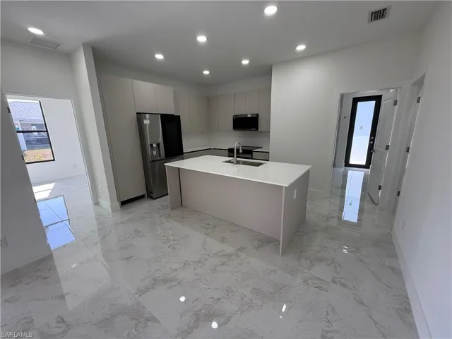 Kitchen with modern cabinets, stainless steel appliances, a center island with sink, gray cabinets, and recessed lighting