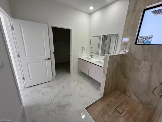 Full bathroom featuring double vanity, a walk in closet, recessed lighting, and light marble finish flooring