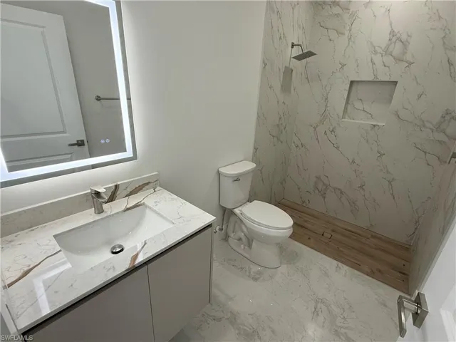 Full bath featuring vanity, a marble finish shower, and light marble finish floors