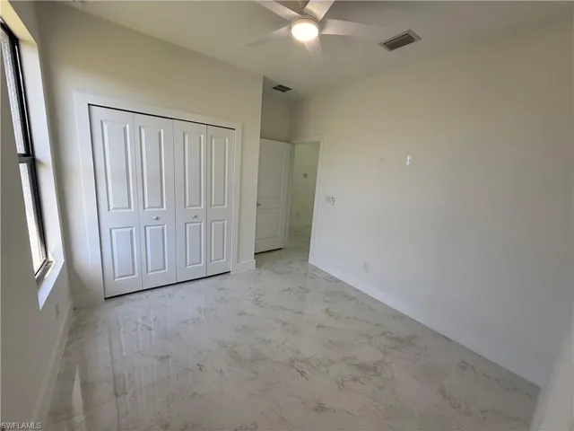 Unfurnished bedroom featuring a ceiling fan, light marble finish flooring, and a closet