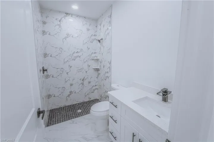 Bathroom with vanity, toilet, a tile shower, and tile patterned floors