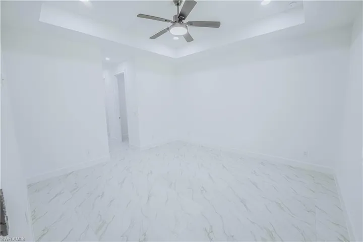Spare room with ceiling fan, a tray ceiling, and light tile patterned floors