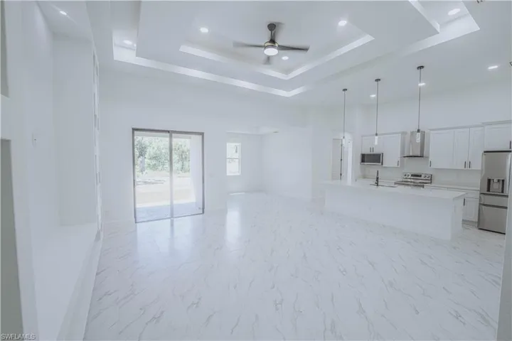 Unfurnished living room featuring light tile patterned flooring, ceiling fan, sink, and a tray ceiling