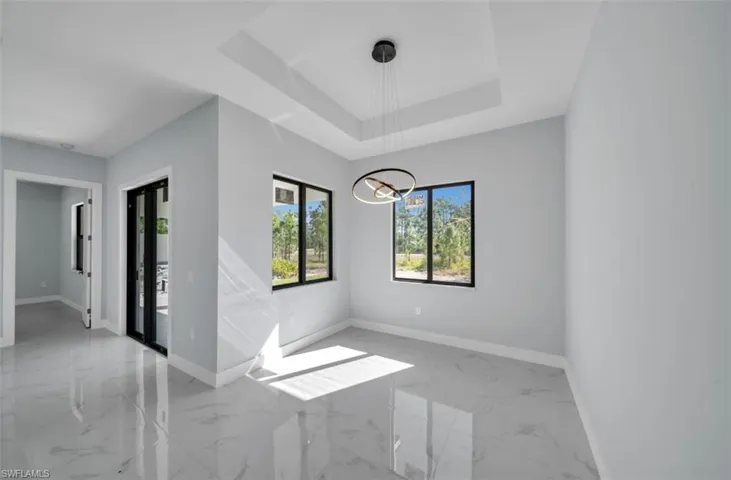 Empty room featuring light marble finish flooring, a tray ceiling, and suspended lighting
