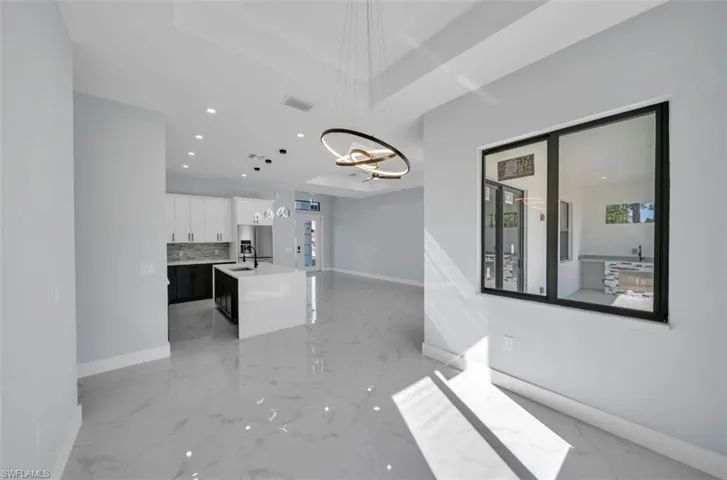 Two tone kitchen featuring light stone countertops, decorative light fixtures, an island with sink, stainless steel refrigerator with ice dispenser, and open floor plan