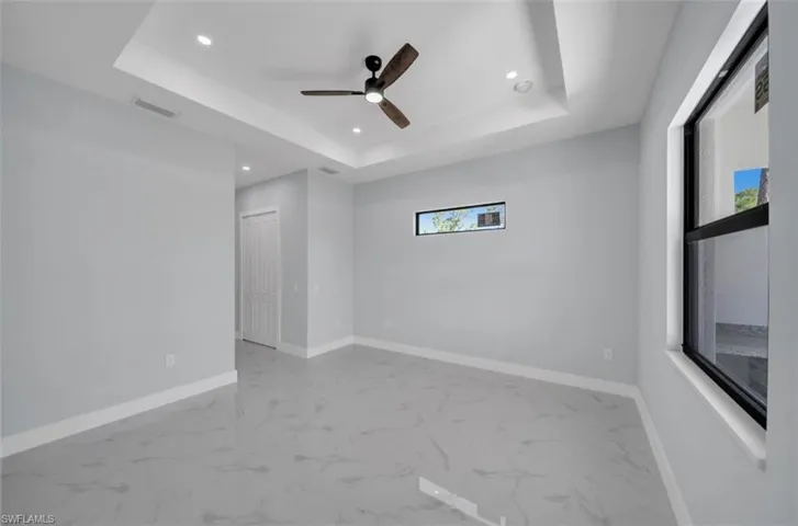 Empty room with recessed lighting, ceiling fan, healthy amount of natural light, a raised ceiling, and light marble finish flooring