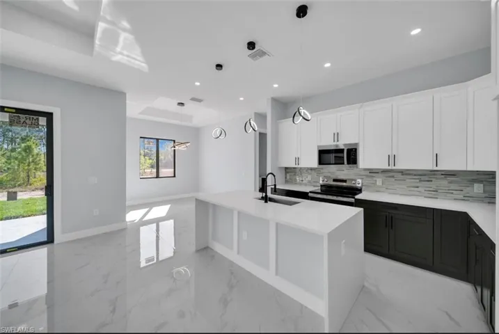 Two tone kitchen featuring dual tone cabinets, decorative light fixtures, stainless steel appliances, an island with sink, and light stone countertops