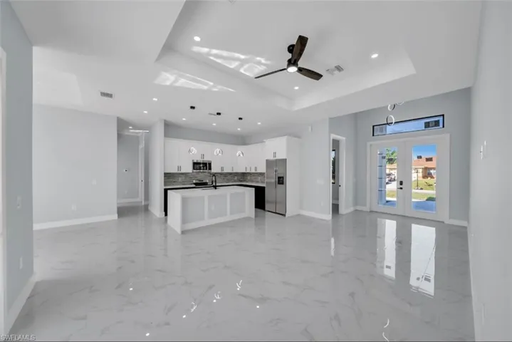 Kitchen with open floor plan, a kitchen island with sink, white cabinets, stainless steel appliances, and a ceiling fan