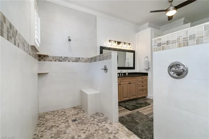 Bathroom with vanity, ornamental molding, tiled shower, and ceiling fan