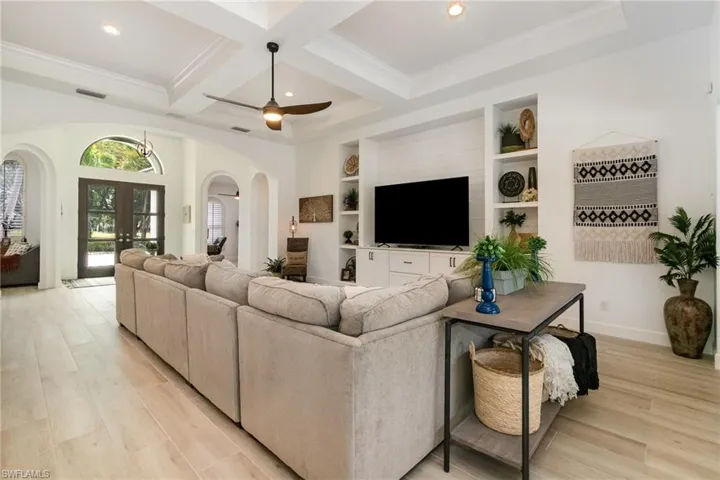 Living area with coffered ceiling, french doors, light wood finished floors, visible vents, and arched walkways