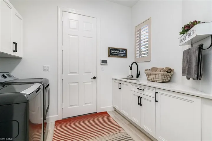 Laundry room featuring light wood-type flooring, baseboards, a sink, cabinet space, and washer and dryer