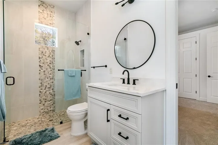 Bathroom with toilet, a stall shower, vanity, and wood finished floors
