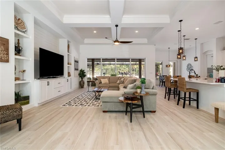 Living area featuring coffered ceiling, crown molding, light wood-type flooring, beam ceiling, and a ceiling fan