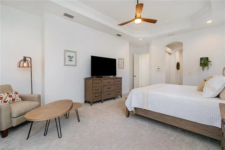 Bedroom featuring arched walkways, ornamental molding, a tray ceiling, and light carpet