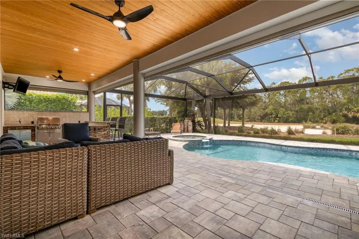 View of swimming pool featuring a pool with connected hot tub, an outdoor kitchen, a ceiling fan, a lanai, and a patio