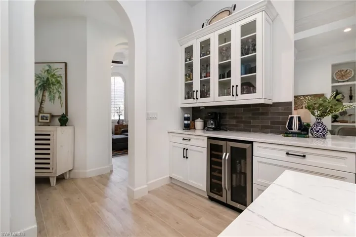 Bar featuring wine cooler, backsplash, light wood-type flooring, baseboards, and arched walkways