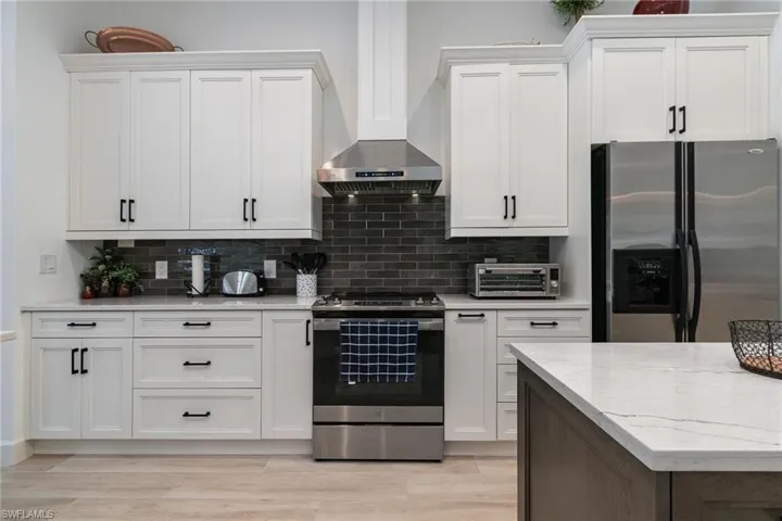 Kitchen with decorative backsplash, stainless steel appliances, a toaster, and wall chimney exhaust hood
