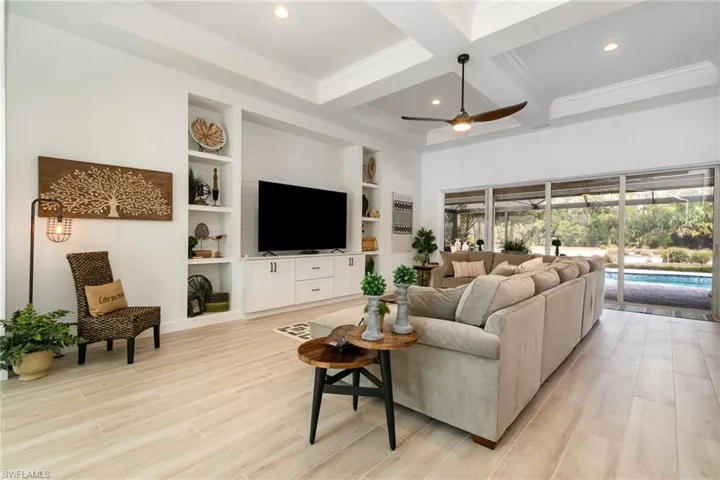 Living area with coffered ceiling, crown molding, beam ceiling, ceiling fan, and light wood-style flooring