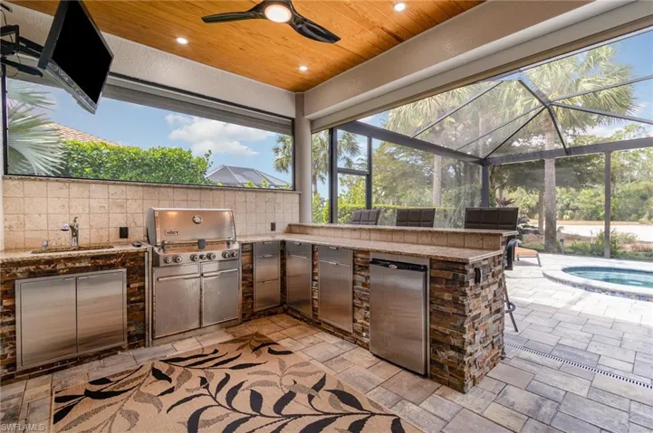 View of patio featuring glass enclosure, a grill, a sink, and an outdoor kitchen