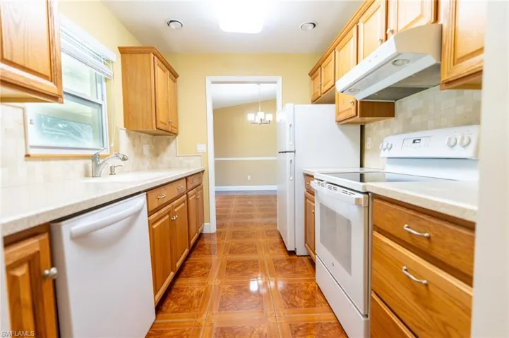 Kitchen featuring tasteful backsplash, white appliances, under cabinet range hood, and a chandelier