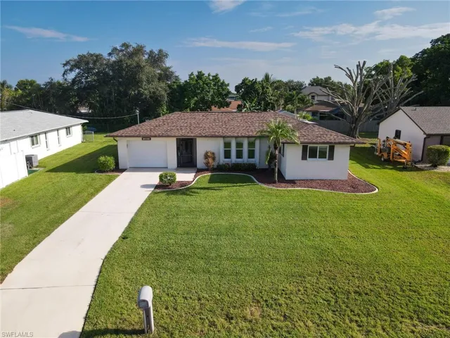 Single story home with beautifully manicured landscaping, featuring a garage, concrete driveway, a front lawn, stucco siding, and a shingled roof