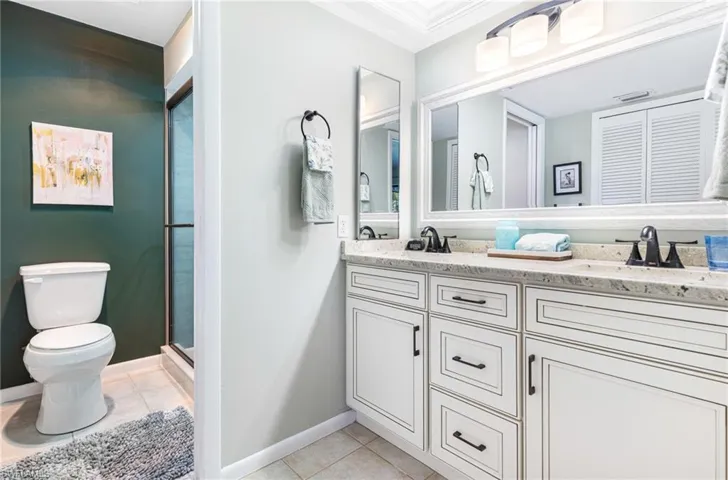 Bathroom with tile patterned flooring, a shower with door, toilet, dual vanity, and ornamental molding