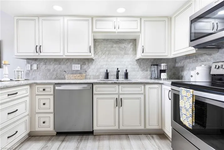 Kitchen with tasteful backsplash, white cabinets, light hardwood / wood-style floors, appliances with stainless steel finishes, and sink