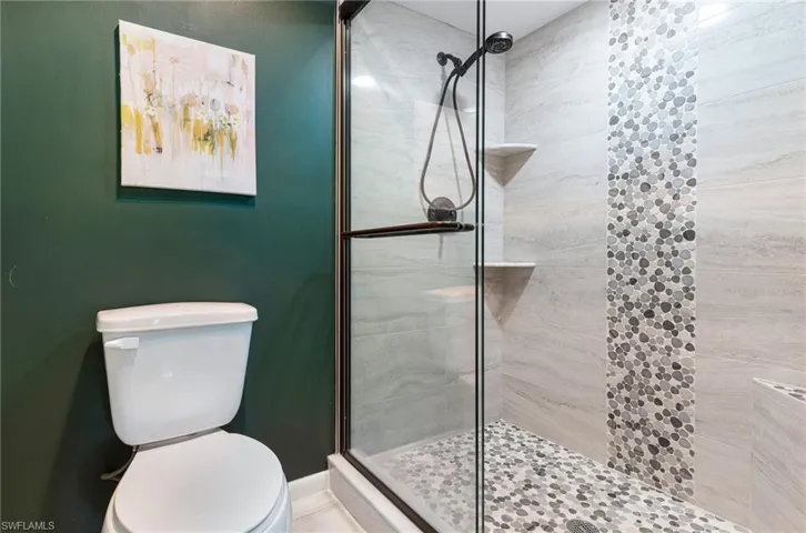 Bathroom featuring a shower with door and toilet