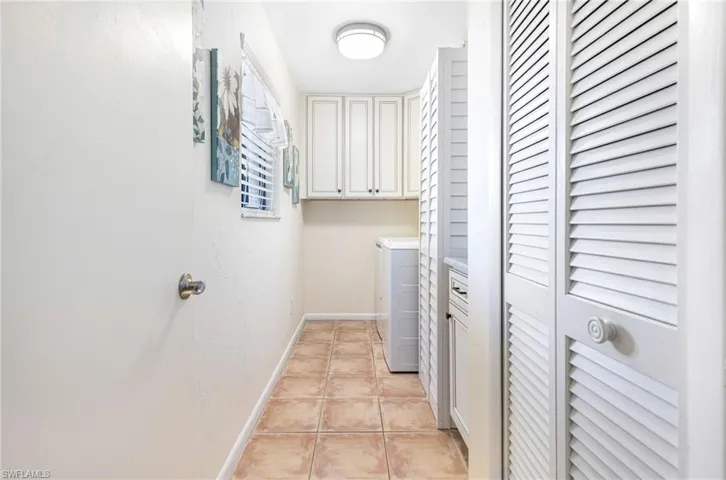 Laundry area with light tile patterned floors, washer and dryer, and cabinets