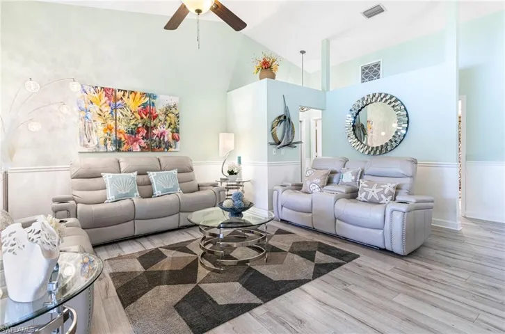 Living room with ceiling fan, light wood-type flooring, and high vaulted ceiling